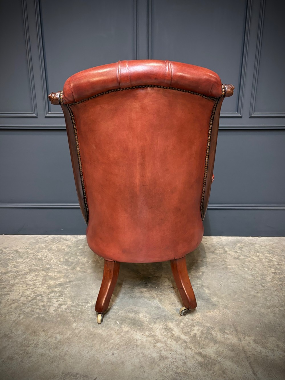 A pair of Victorian library armchairs upholstered in deep-buttoned reddish-brown leather with carved mahogany frames and brass castors. View XIV