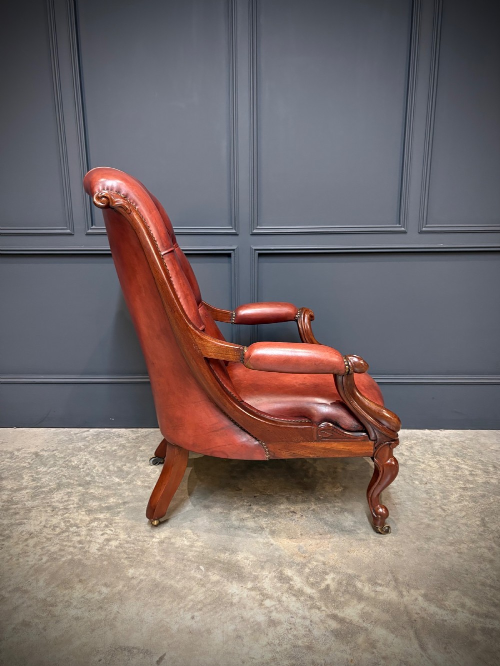 A pair of Victorian library armchairs upholstered in deep-buttoned reddish-brown leather with carved mahogany frames and brass castors. View XV