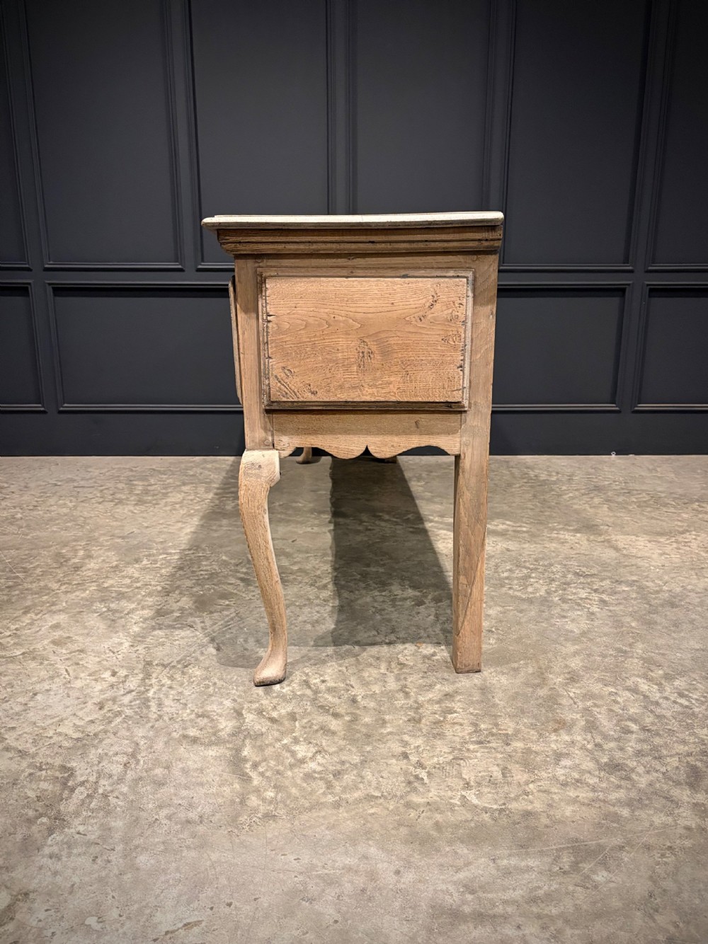 An 18th-century carved oak dresser base featuring three drawers with detailed relief carving, brass handles, shaped apron, cabriole front legs, and a pale bleached finish. View III