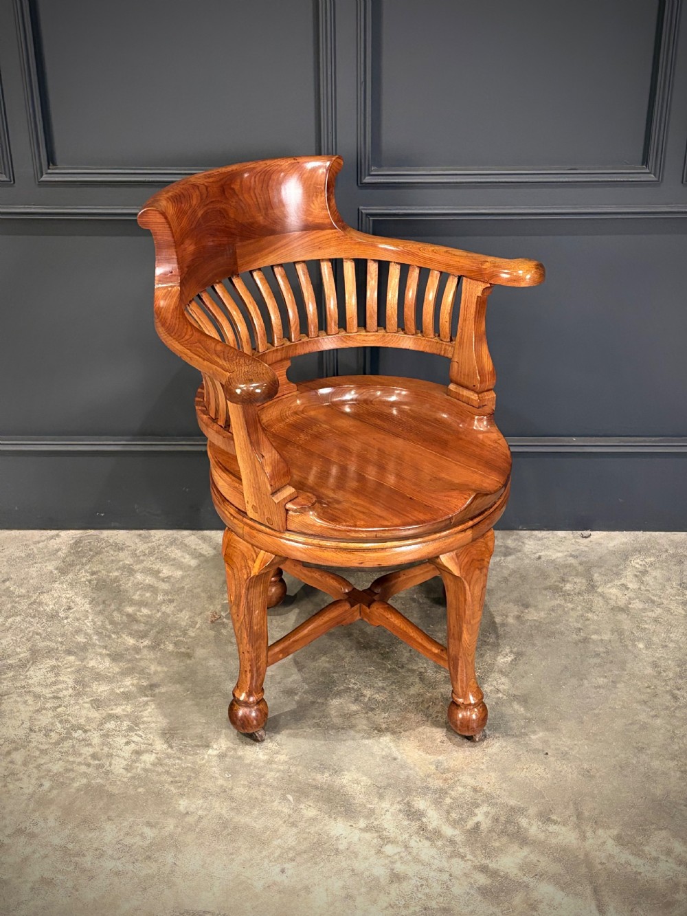 A solid walnut swivel desk chair featuring a curved horseshoe backrest with vertical slats, a contoured saddle seat, and four shaped legs on castors. View II