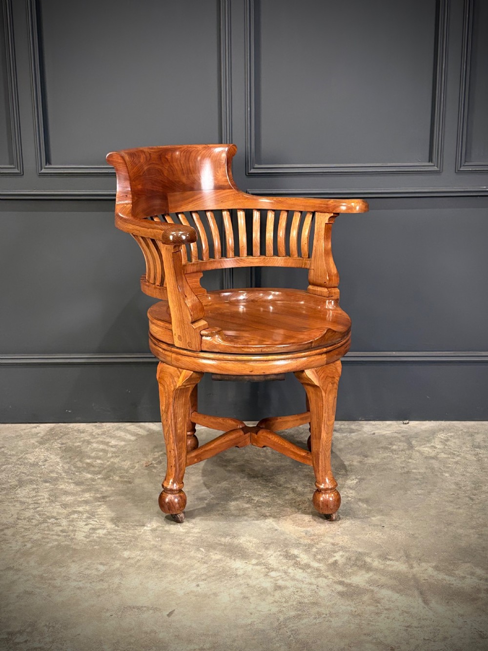 A solid walnut swivel desk chair featuring a curved horseshoe backrest with vertical slats, a contoured saddle seat, and four shaped legs on castors.