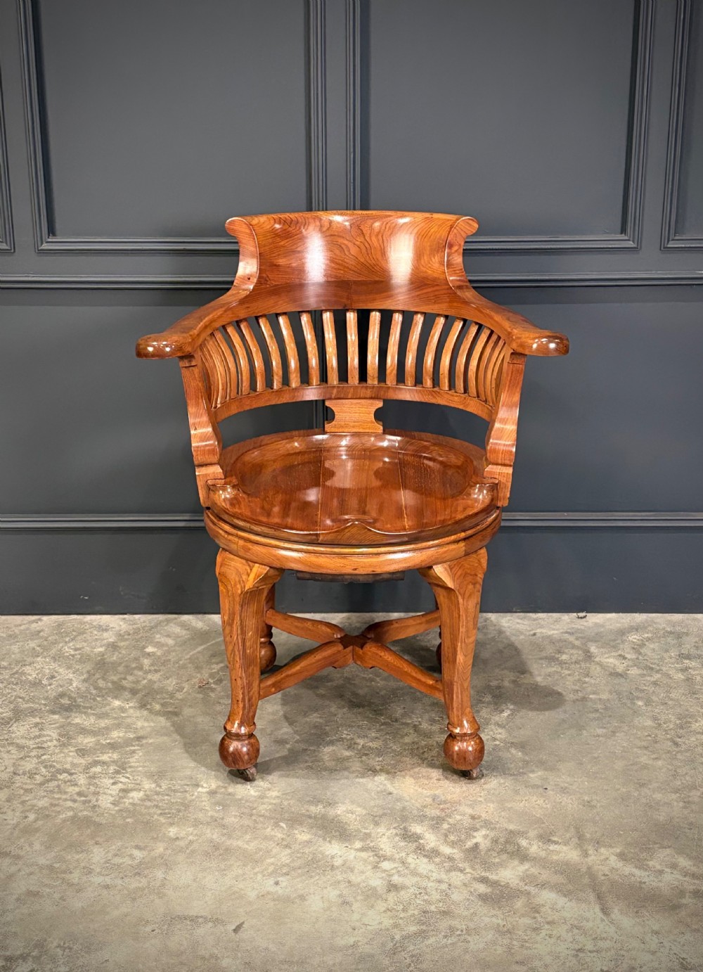A solid walnut swivel desk chair featuring a curved horseshoe backrest with vertical slats, a contoured saddle seat, and four shaped legs on castors. View III