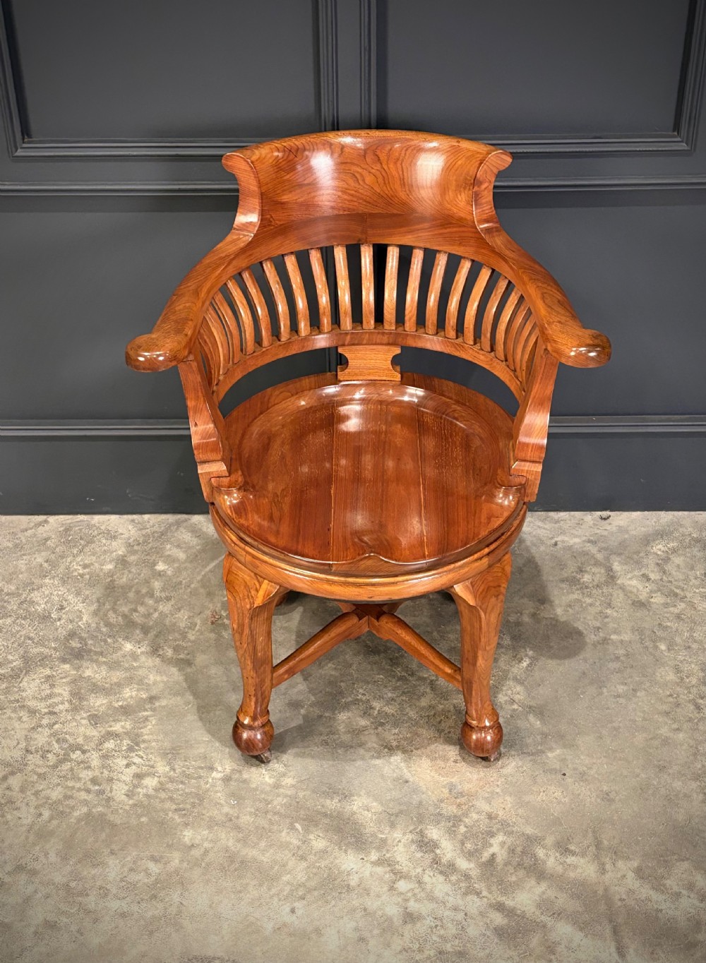 A solid walnut swivel desk chair featuring a curved horseshoe backrest with vertical slats, a contoured saddle seat, and four shaped legs on castors. View IV