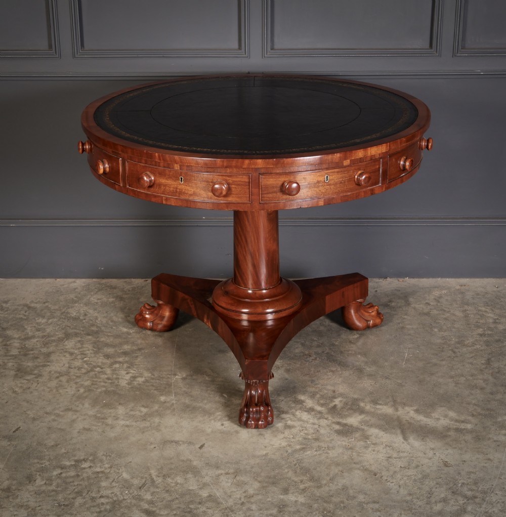 A circular William IV mahogany rotating drum table featuring a black leather inset top, frieze drawers with turned handles, a thick turned column, and a triform base with carved paw feet.