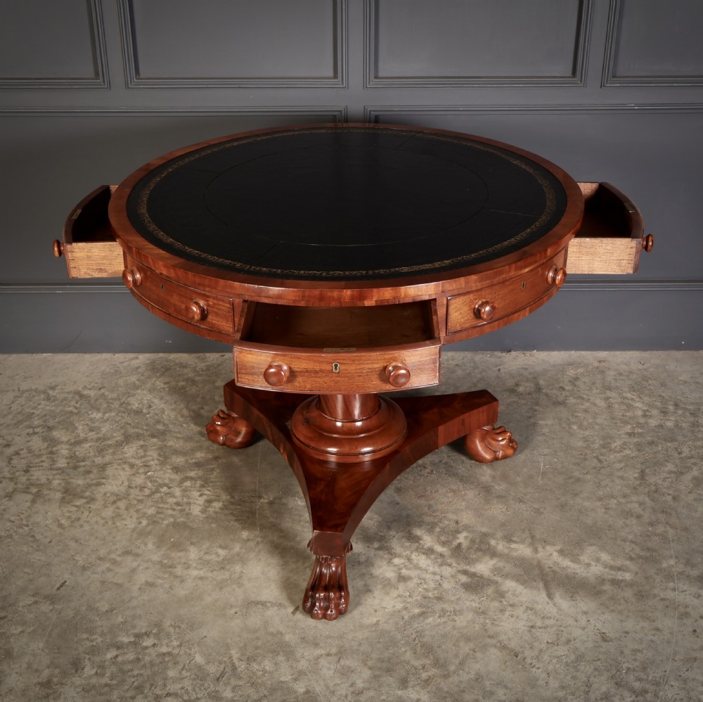 A circular William IV mahogany rotating drum table featuring a black leather inset top, frieze drawers with turned handles, a thick turned column, and a triform base with carved paw feet. View II