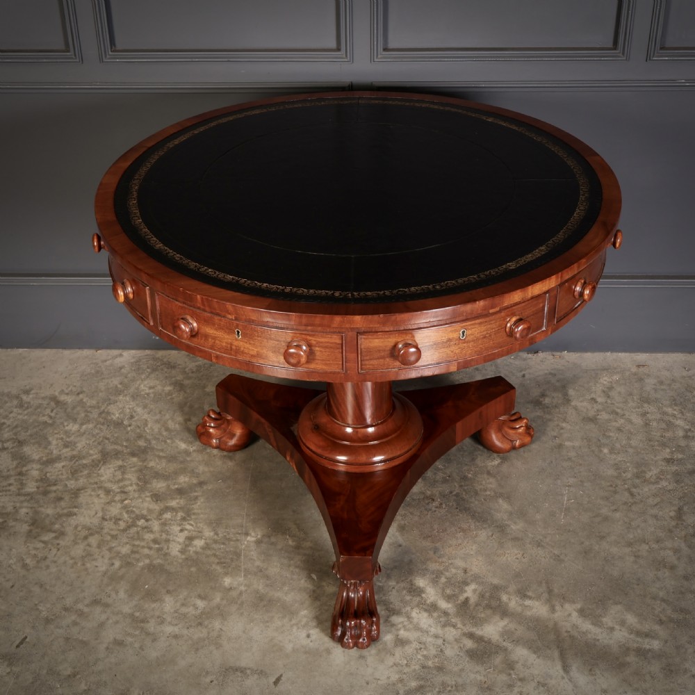A circular William IV mahogany rotating drum table featuring a black leather inset top, frieze drawers with turned handles, a thick turned column, and a triform base with carved paw feet. View III