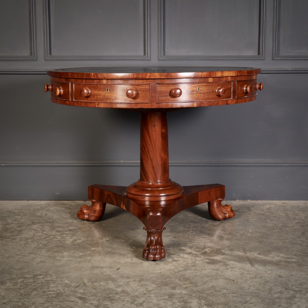 A circular William IV mahogany rotating drum table featuring a black leather inset top, frieze drawers with turned handles, a thick turned column, and a triform base with carved paw feet. View IV