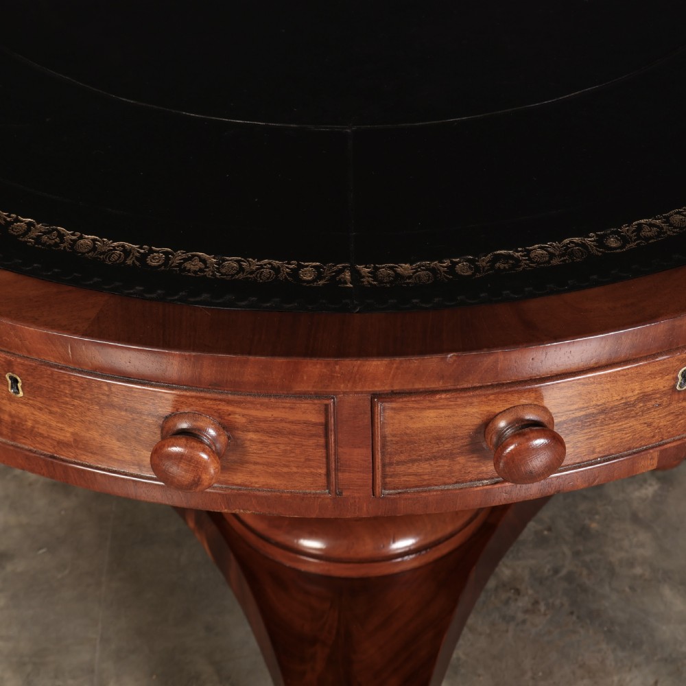 A circular William IV mahogany rotating drum table featuring a black leather inset top, frieze drawers with turned handles, a thick turned column, and a triform base with carved paw feet. View VI