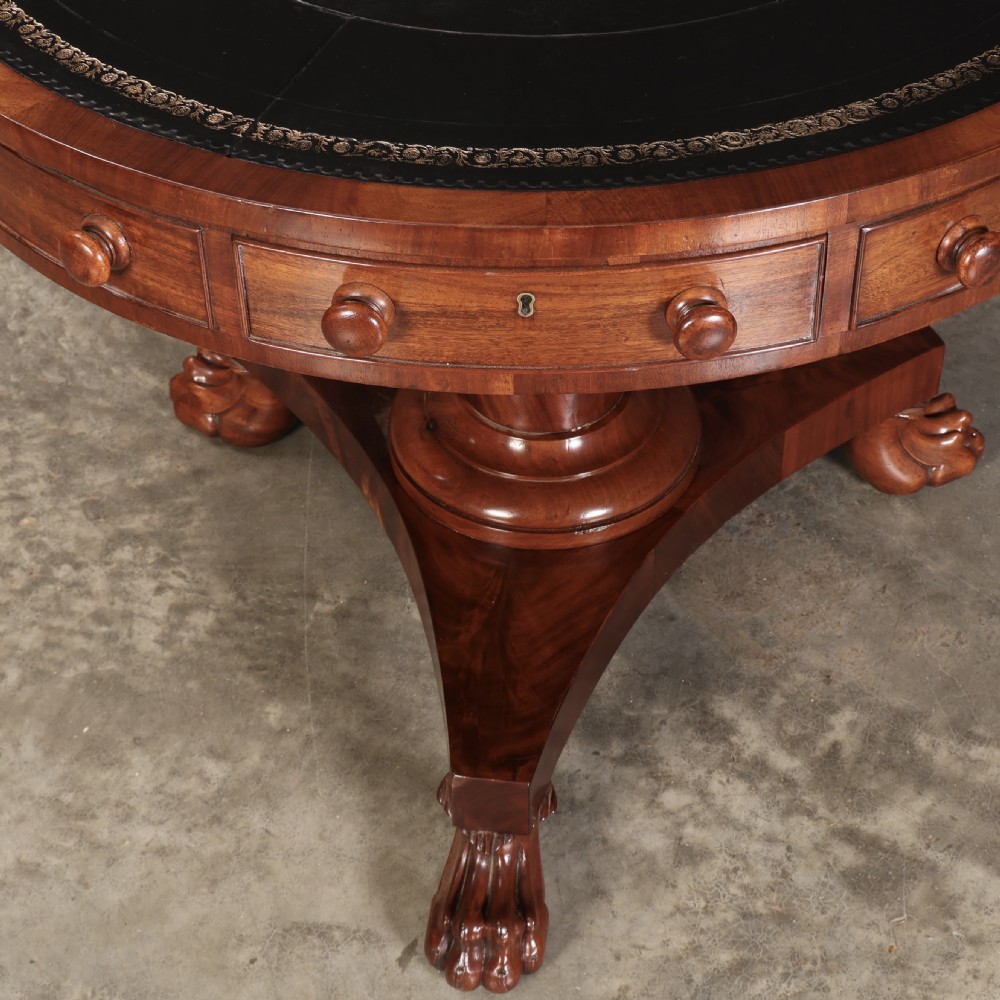 A circular William IV mahogany rotating drum table featuring a black leather inset top, frieze drawers with turned handles, a thick turned column, and a triform base with carved paw feet. View IX