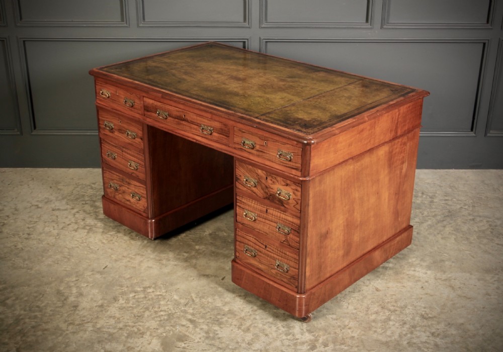 A nineteenth-century Victorian walnut pedestal desk featuring an inset green leather writing surface, twin drawer pedestals, and brass drop handles.