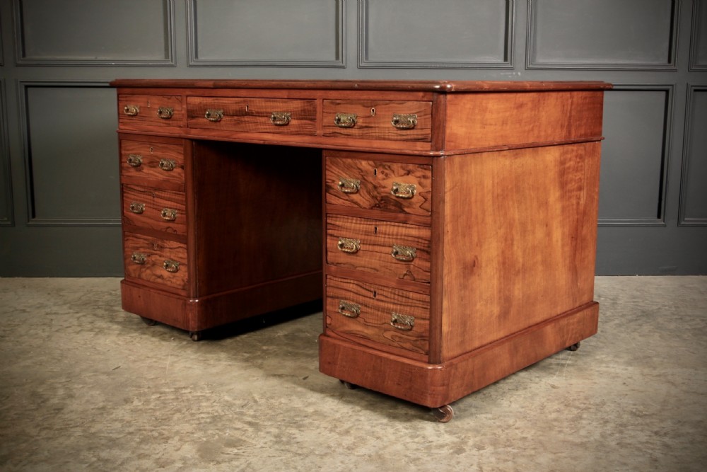 A nineteenth-century Victorian walnut pedestal desk featuring an inset green leather writing surface, twin drawer pedestals, and brass drop handles. View VI