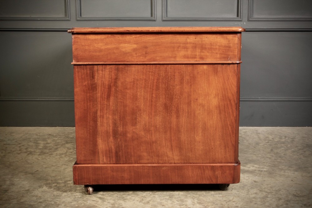 A nineteenth-century Victorian walnut pedestal desk featuring an inset green leather writing surface, twin drawer pedestals, and brass drop handles. View X