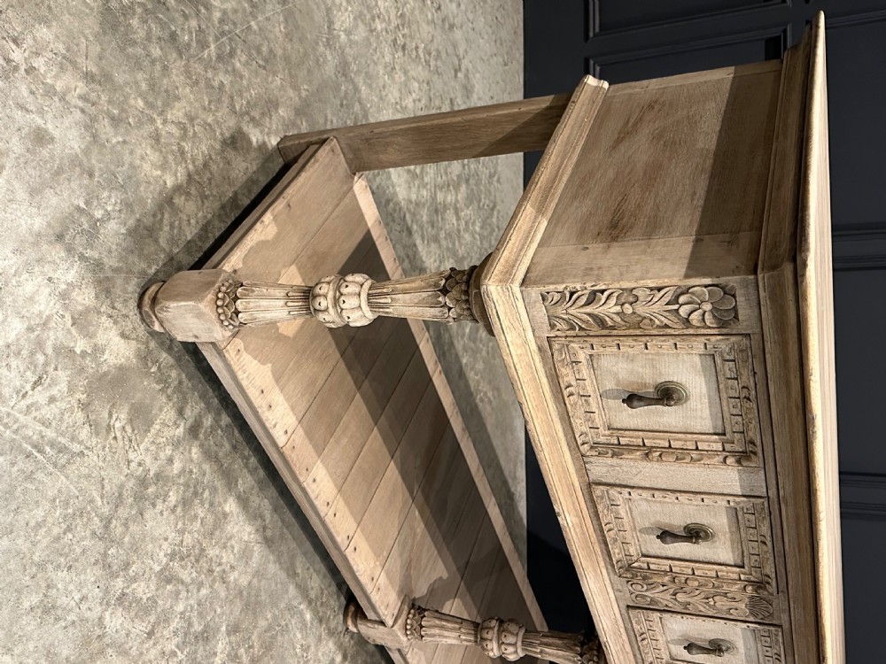 A long carved bleached oak potboard dresser base featuring relief carved drawer fronts, turned support legs, brass drop handles, and an open lower display shelf. View III