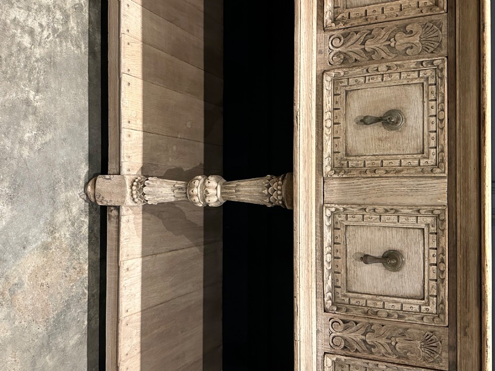 A long carved bleached oak potboard dresser base featuring relief carved drawer fronts, turned support legs, brass drop handles, and an open lower display shelf. View VII