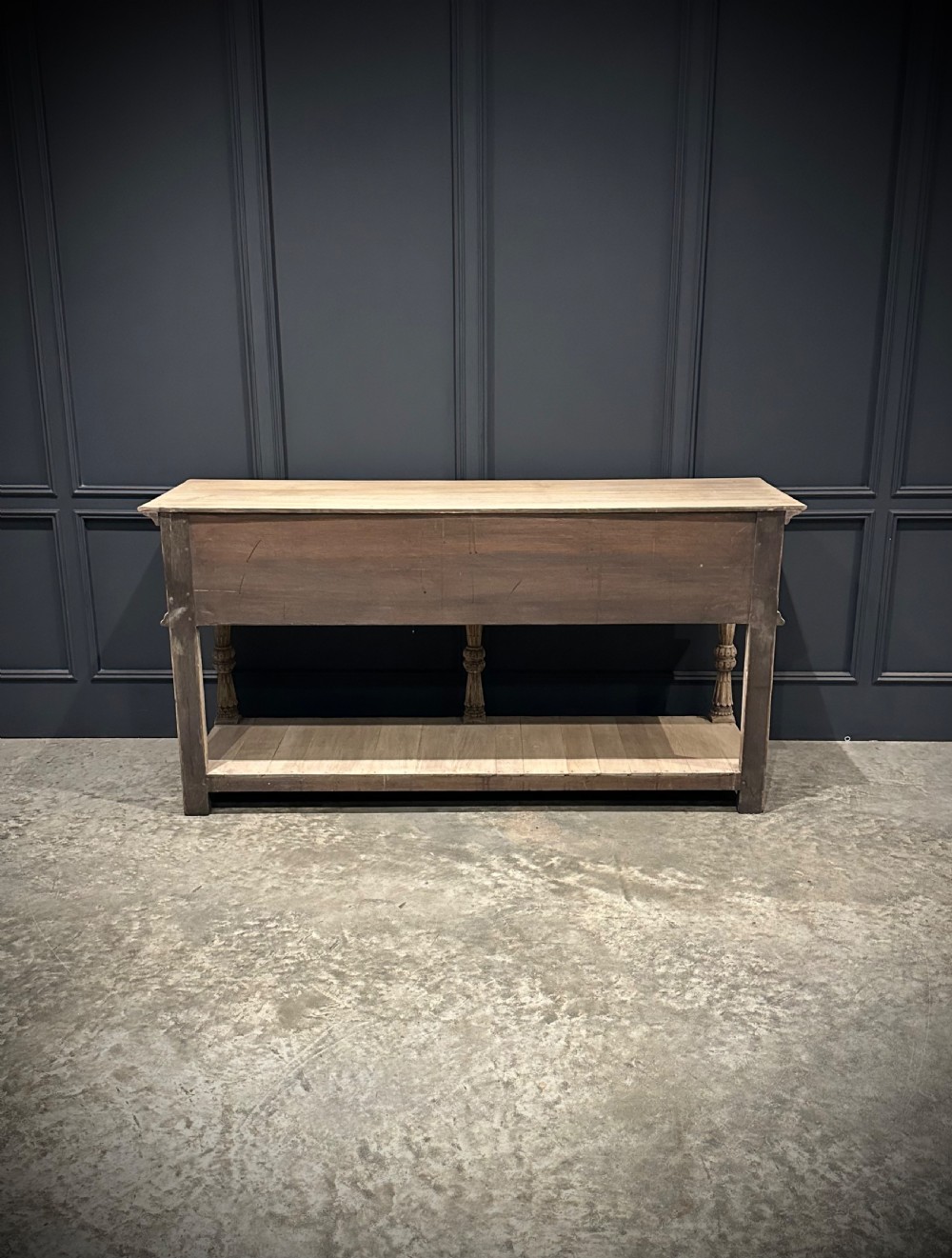 A long carved bleached oak potboard dresser base featuring relief carved drawer fronts, turned support legs, brass drop handles, and an open lower display shelf. View XIII