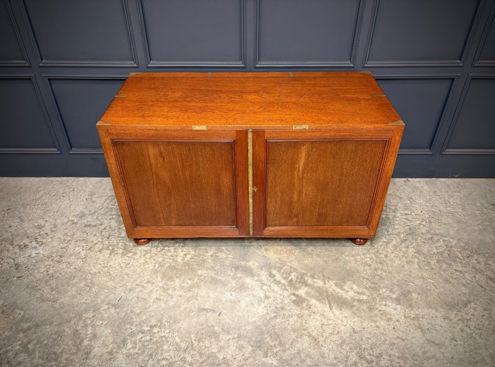 A low Victorian teak military campaign side cabinet featuring double panelled doors, brass corner mounts, brass side handles, and short turned feet. View III