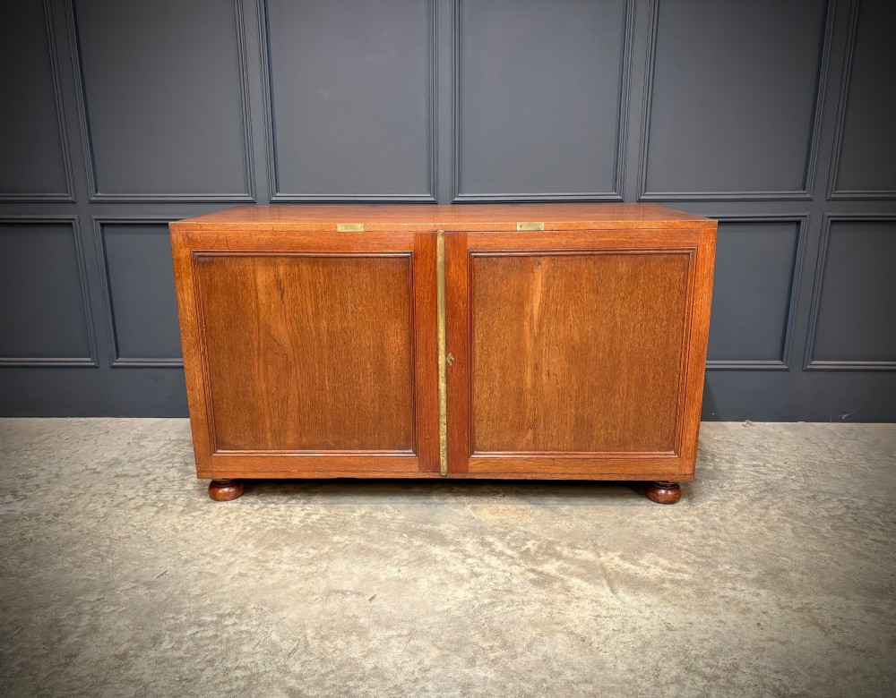 A low Victorian teak military campaign side cabinet featuring double panelled doors, brass corner mounts, brass side handles, and short turned feet. View IV