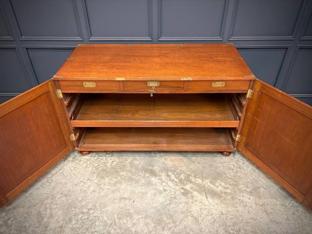 A low Victorian teak military campaign side cabinet featuring double panelled doors, brass corner mounts, brass side handles, and short turned feet. View VI