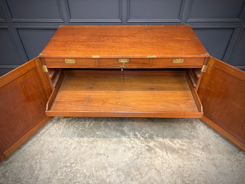 A low Victorian teak military campaign side cabinet featuring double panelled doors, brass corner mounts, brass side handles, and short turned feet. View VII