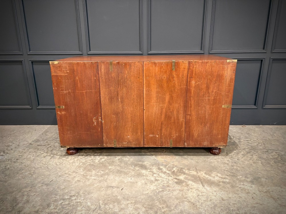 A low Victorian teak military campaign side cabinet featuring double panelled doors, brass corner mounts, brass side handles, and short turned feet. View XI