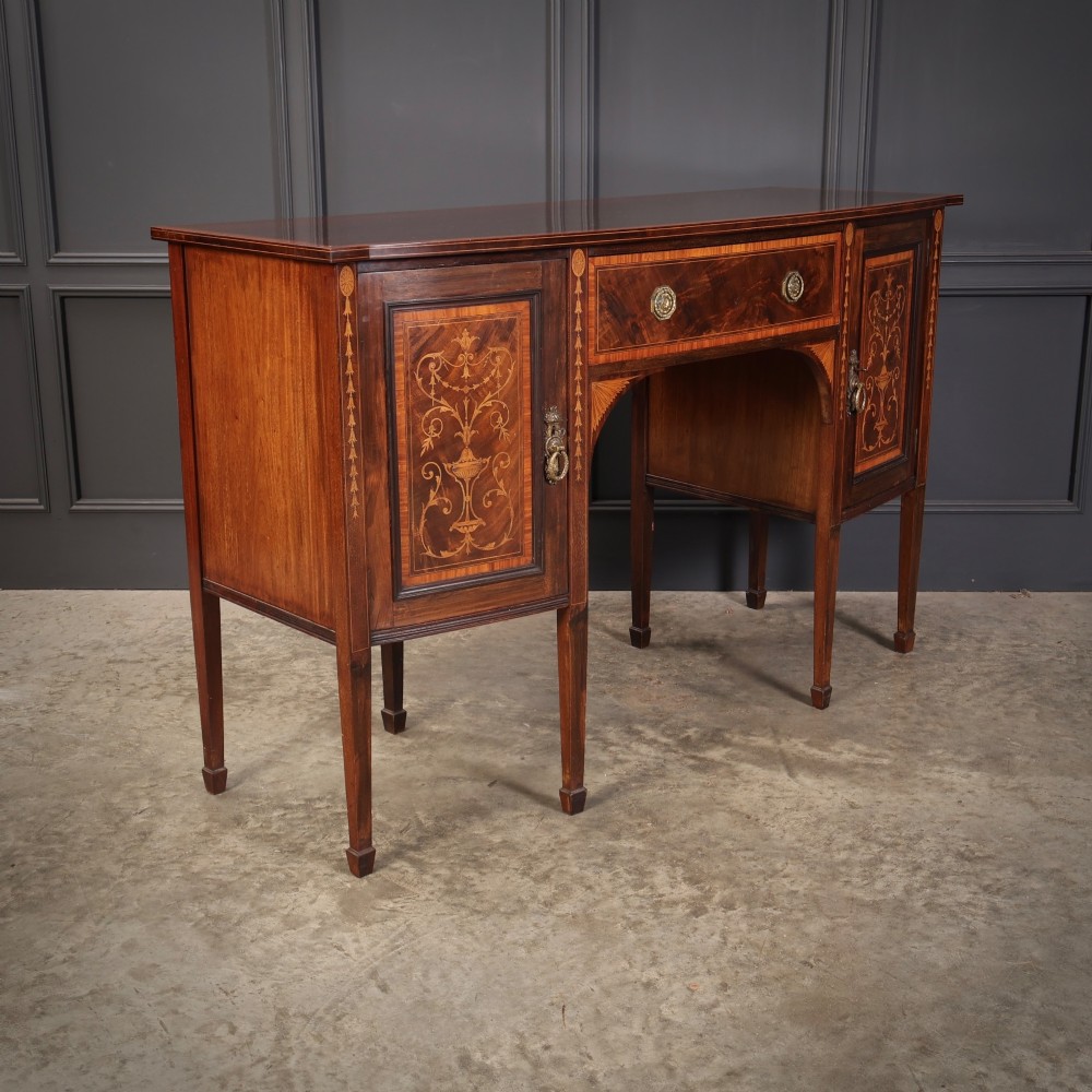 An antique bowfront mahogany sideboard featuring intricate urn marquetry inlays on cupboard doors, a central drawer, and slender square tapered legs. View II