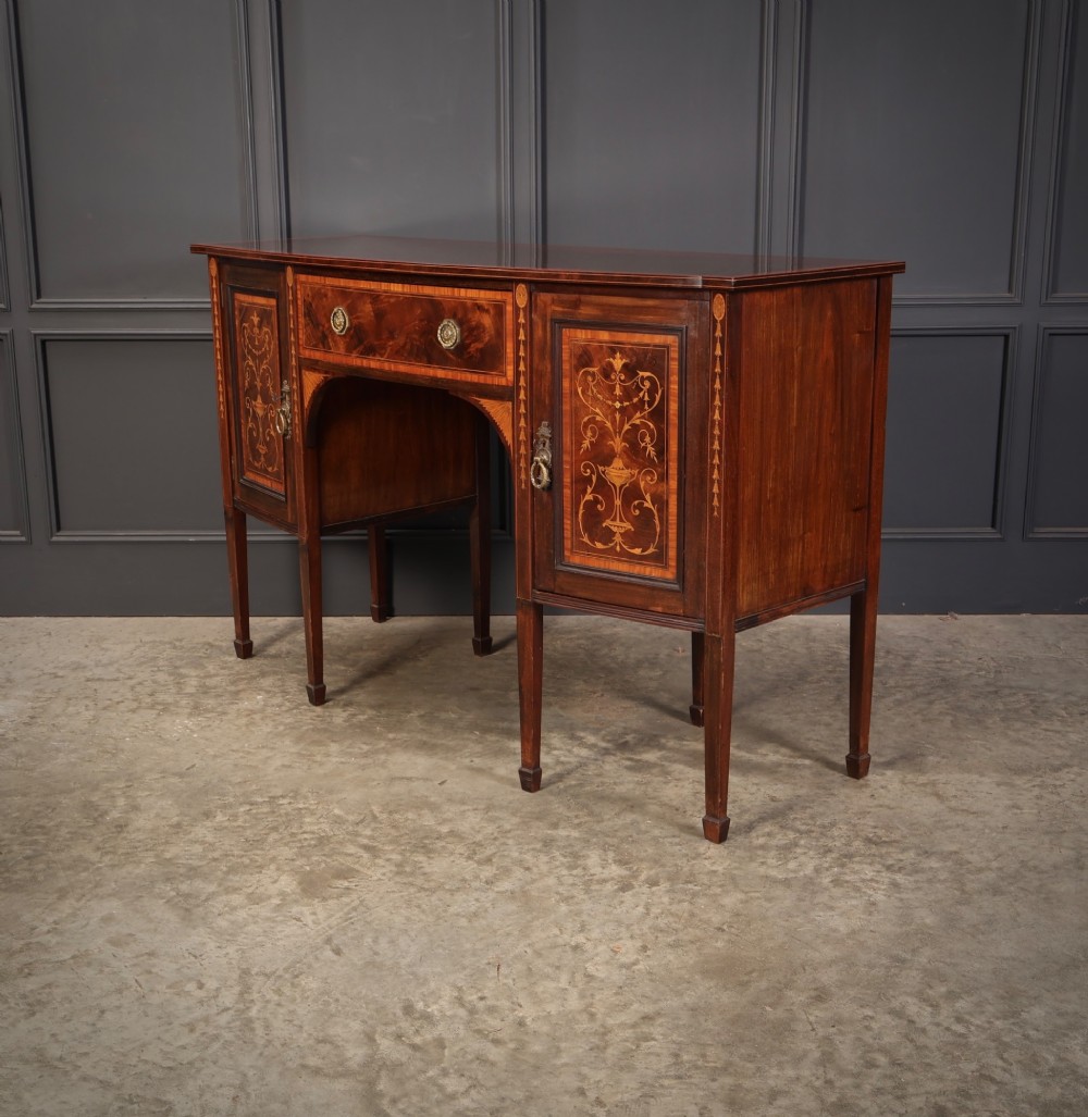 An antique bowfront mahogany sideboard featuring intricate urn marquetry inlays on cupboard doors, a central drawer, and slender square tapered legs. View IX