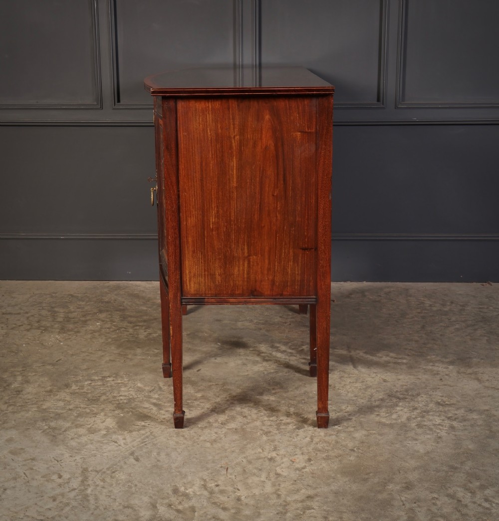 An antique bowfront mahogany sideboard featuring intricate urn marquetry inlays on cupboard doors, a central drawer, and slender square tapered legs. View XI