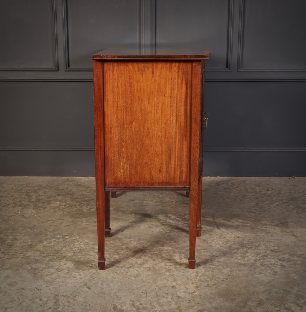 An antique bowfront mahogany sideboard featuring intricate urn marquetry inlays on cupboard doors, a central drawer, and slender square tapered legs. View XIII