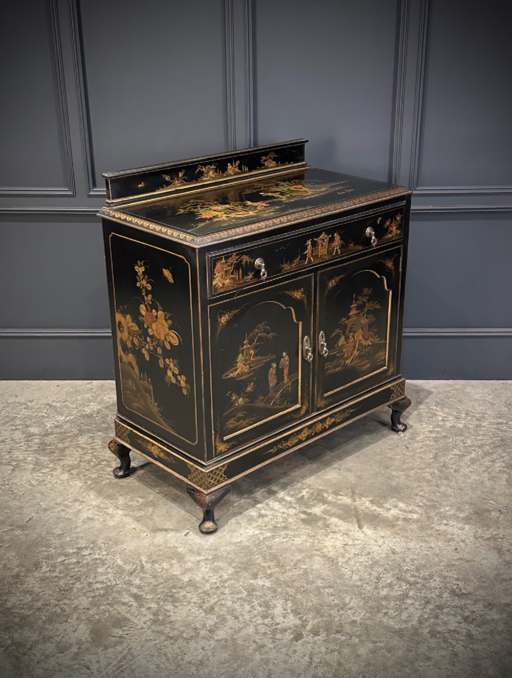 A black lacquered side cabinet decorated with gold chinoiserie landscape scenes, featuring one top drawer, double doors, and cabriole legs. View II
