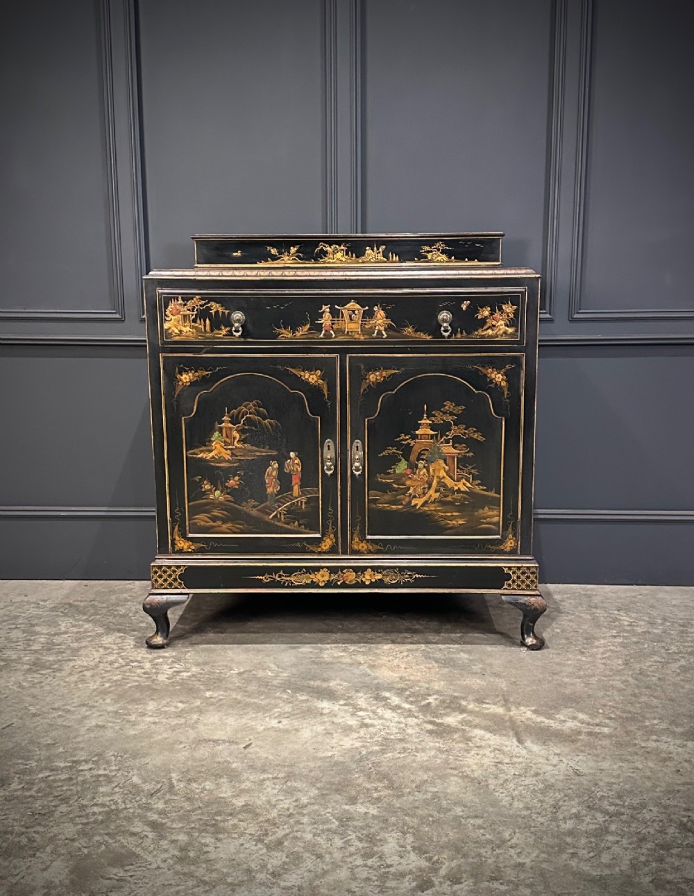 A black lacquered side cabinet decorated with gold chinoiserie landscape scenes, featuring one top drawer, double doors, and cabriole legs. View III