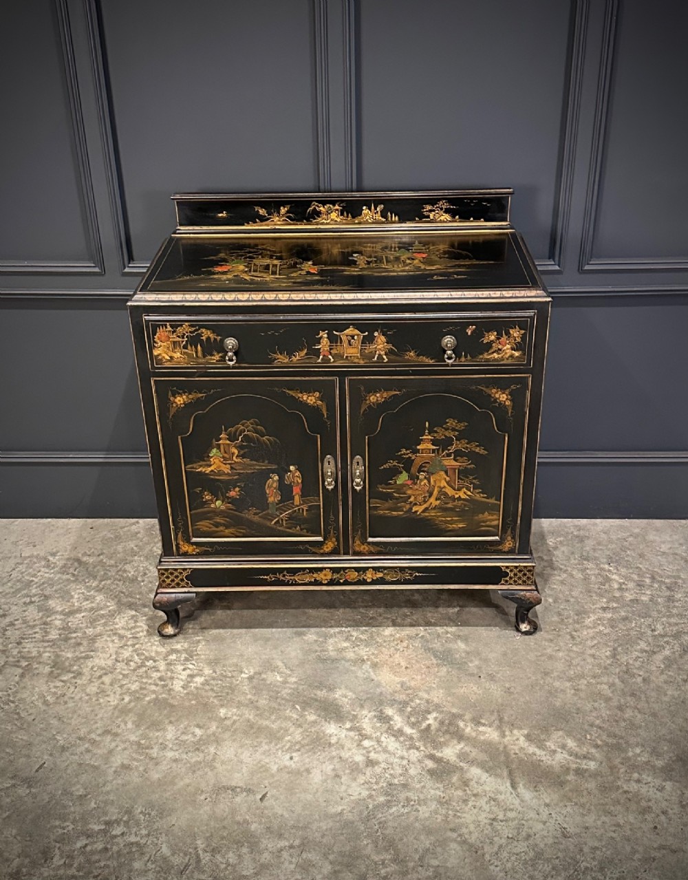 A black lacquered side cabinet decorated with gold chinoiserie landscape scenes, featuring one top drawer, double doors, and cabriole legs. View IV