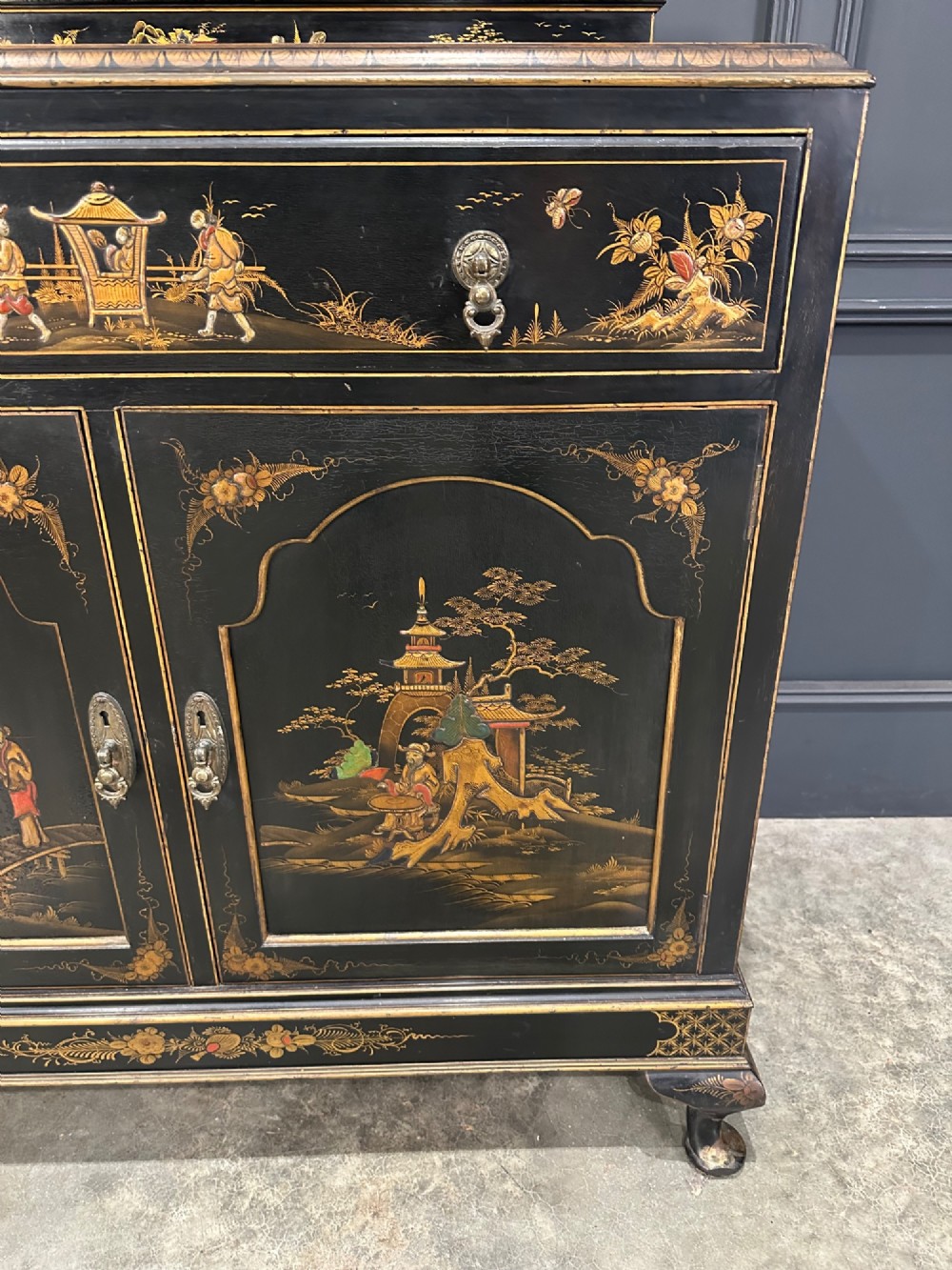 A black lacquered side cabinet decorated with gold chinoiserie landscape scenes, featuring one top drawer, double doors, and cabriole legs. View VI