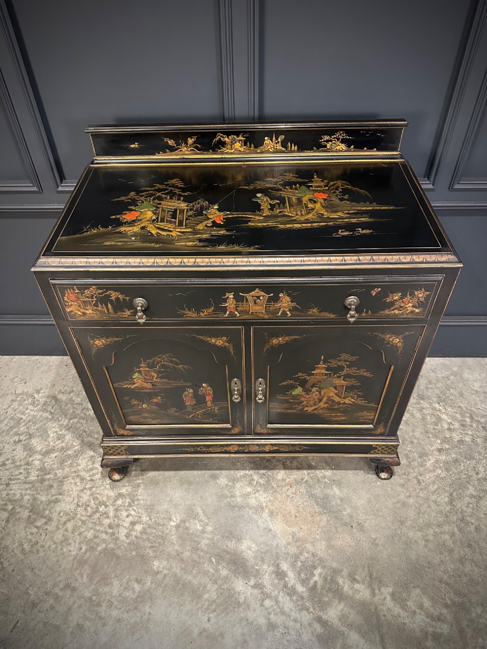 A black lacquered side cabinet decorated with gold chinoiserie landscape scenes, featuring one top drawer, double doors, and cabriole legs. View VII