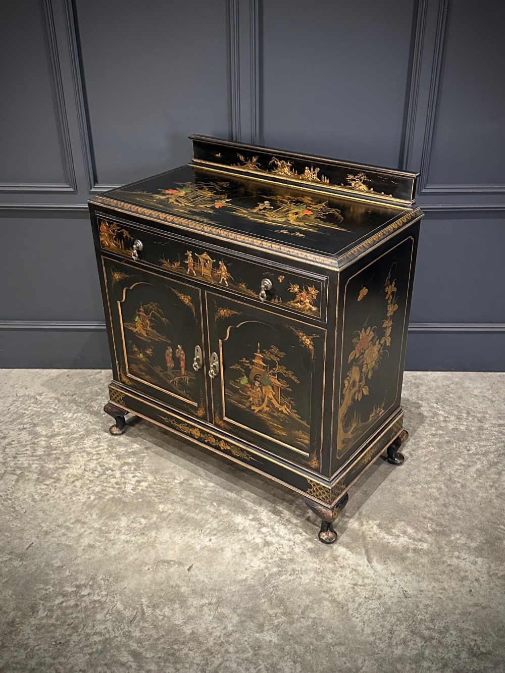 A black lacquered side cabinet decorated with gold chinoiserie landscape scenes, featuring one top drawer, double doors, and cabriole legs. View VIII