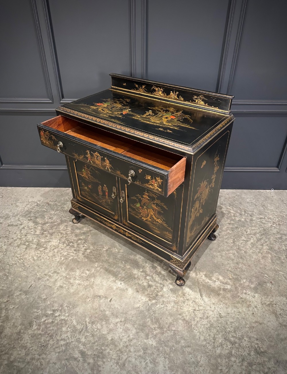 A black lacquered side cabinet decorated with gold chinoiserie landscape scenes, featuring one top drawer, double doors, and cabriole legs. View X