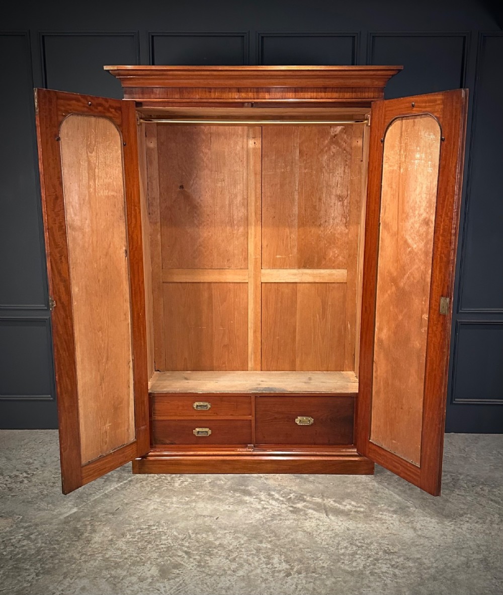 A Victorian mahogany double wardrobe featuring two arched panel doors with carved crest details, a flared top cornice, and a solid plinth base. View III