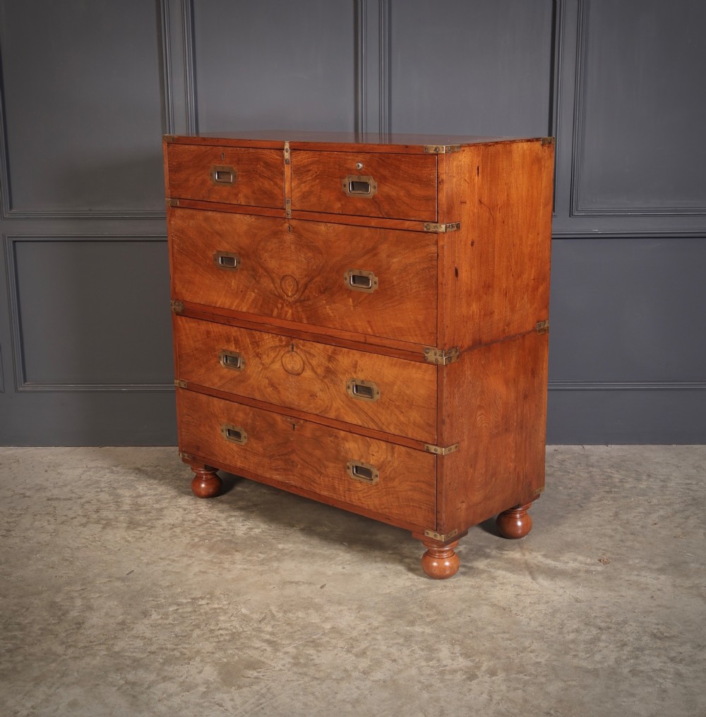A Victorian figured walnut military campaign chest featuring two stackable sections, flush brass handles, brass corner strapping, and turned feet. View VII