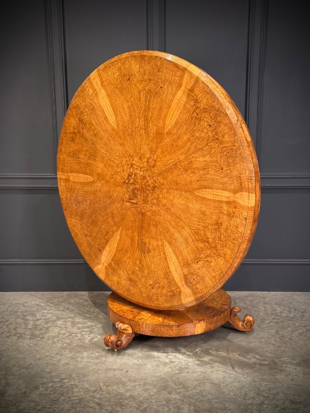 A round antique pollard oak breakfast table featuring a radial veneer pattern, faceted pedestal column, platform base, and four scroll feet. View V