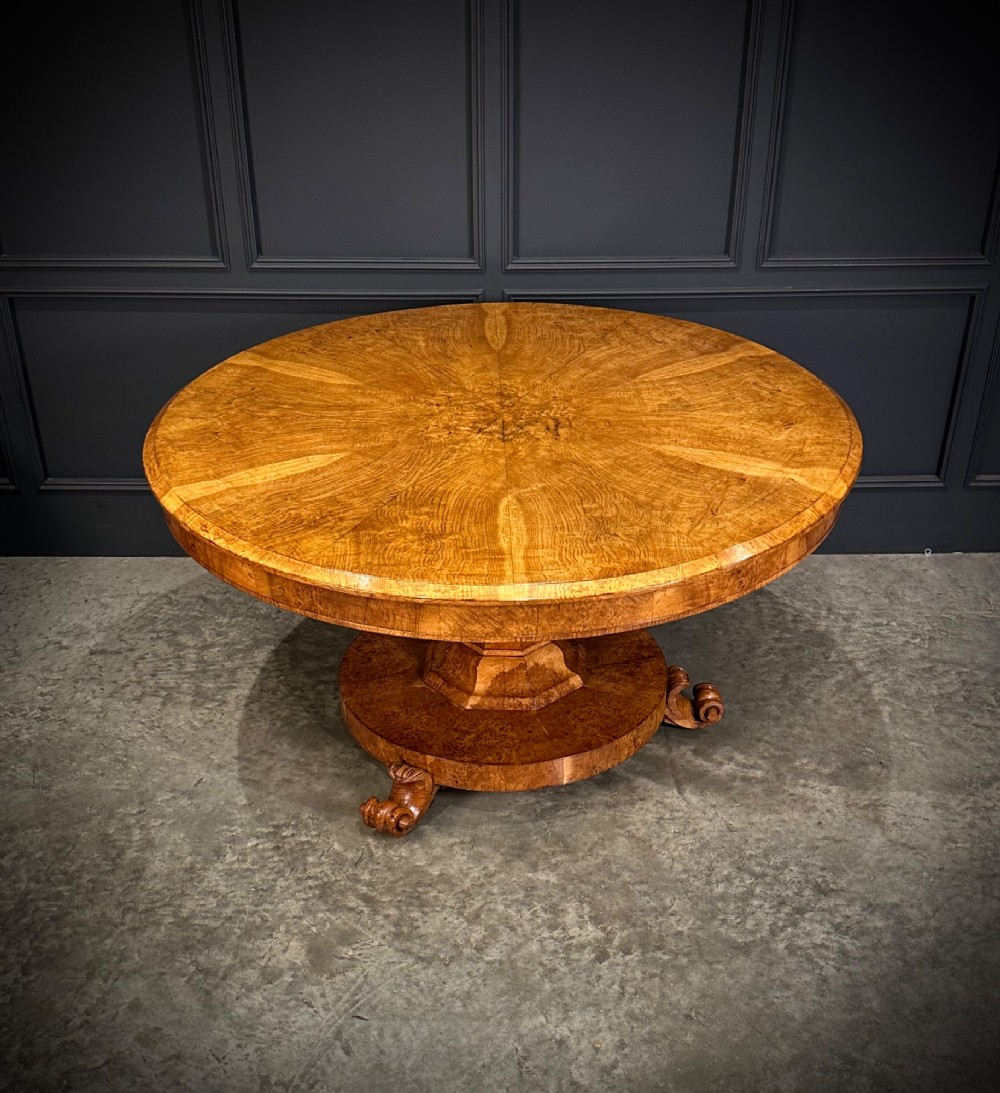 A round antique pollard oak breakfast table featuring a radial veneer pattern, faceted pedestal column, platform base, and four scroll feet.