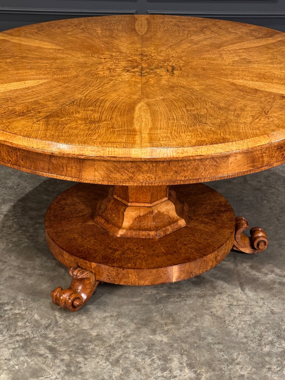 A round antique pollard oak breakfast table featuring a radial veneer pattern, faceted pedestal column, platform base, and four scroll feet. View XII