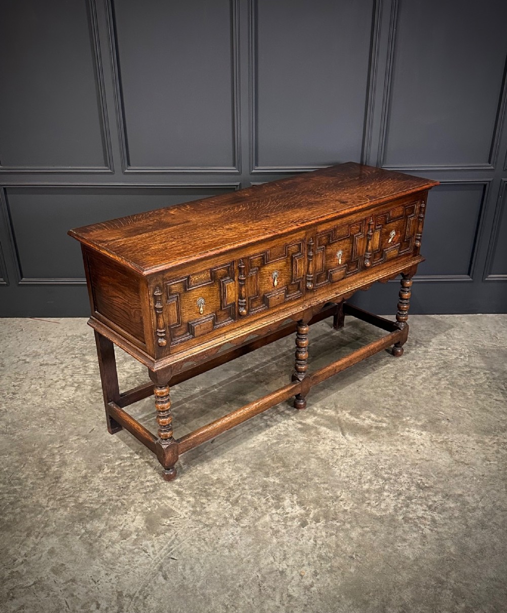 An antique oak dresser base featuring three drawers with geometric panel mouldings, turned front legs, and brass drop handles.