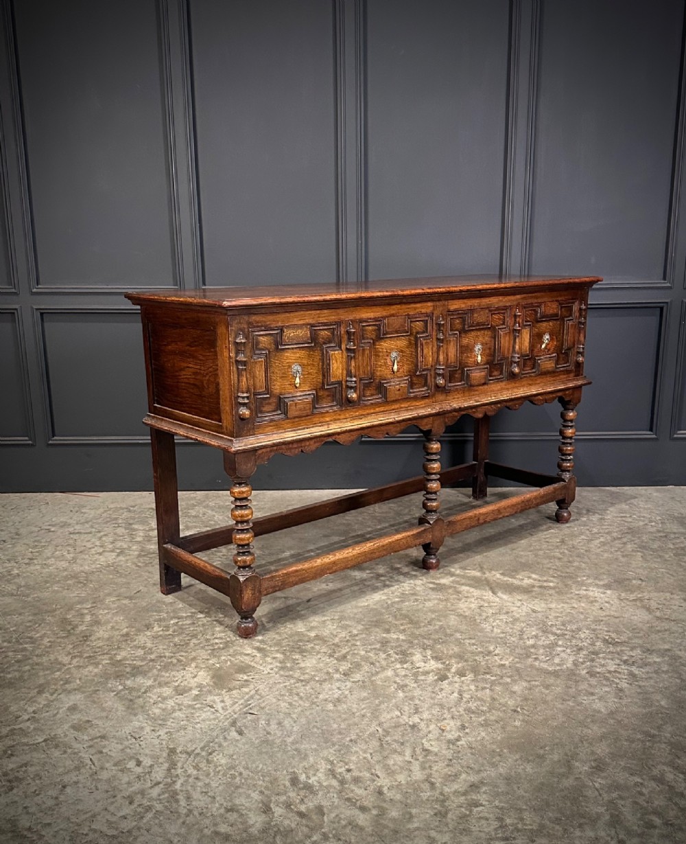 An antique oak dresser base featuring three drawers with geometric panel mouldings, turned front legs, and brass drop handles. View II