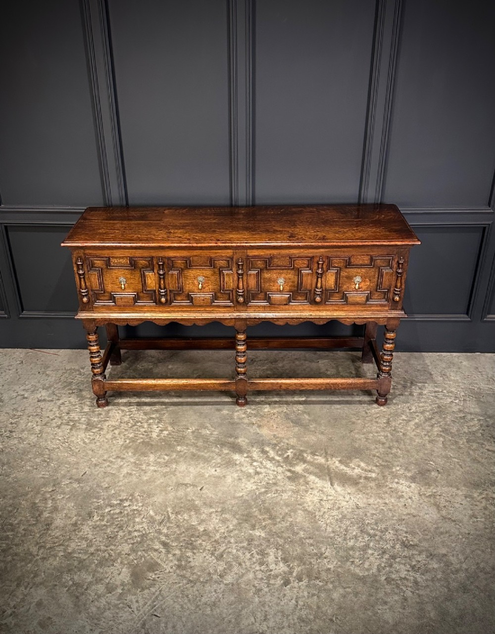 An antique oak dresser base featuring three drawers with geometric panel mouldings, turned front legs, and brass drop handles. View III