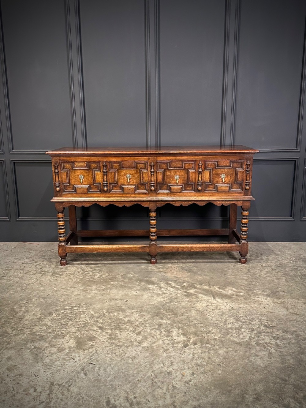 An antique oak dresser base featuring three drawers with geometric panel mouldings, turned front legs, and brass drop handles. View IV
