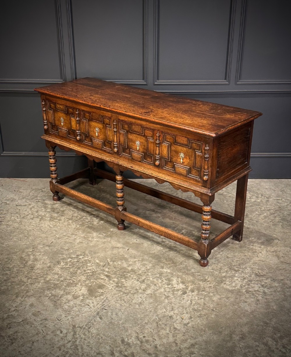 An antique oak dresser base featuring three drawers with geometric panel mouldings, turned front legs, and brass drop handles. View V