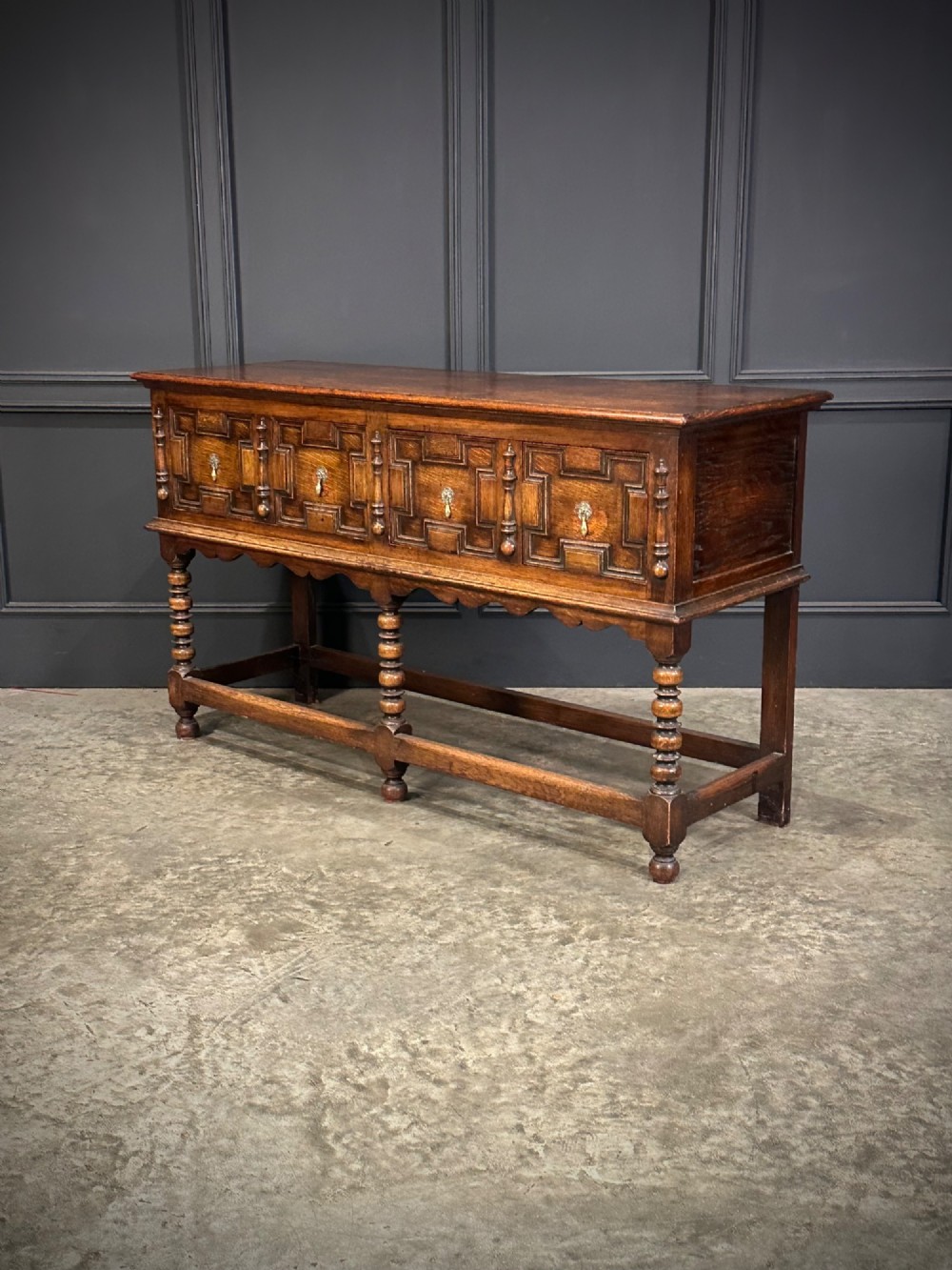 An antique oak dresser base featuring three drawers with geometric panel mouldings, turned front legs, and brass drop handles. View VI