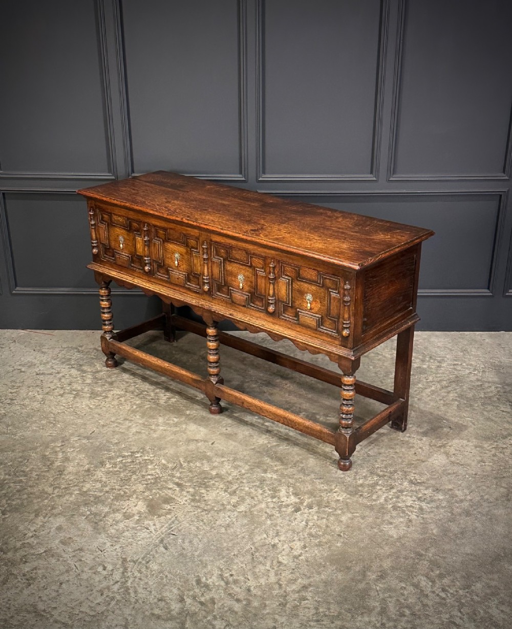 An antique oak dresser base featuring three drawers with geometric panel mouldings, turned front legs, and brass drop handles. View VII
