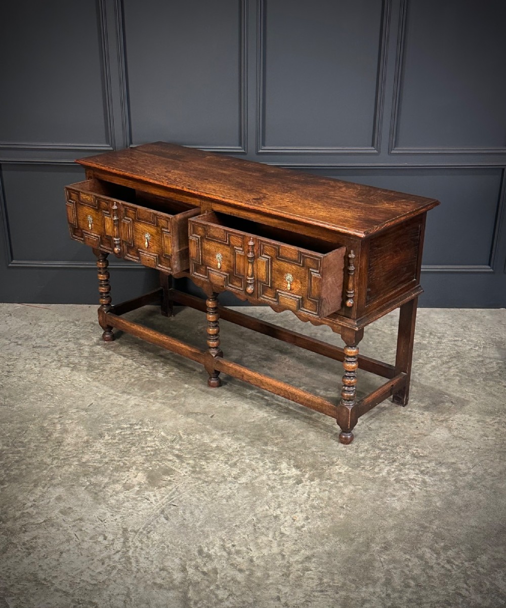 An antique oak dresser base featuring three drawers with geometric panel mouldings, turned front legs, and brass drop handles. View VIII