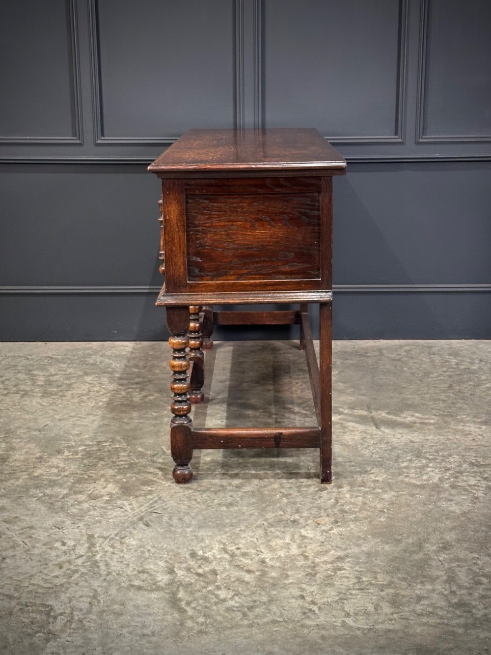 An antique oak dresser base featuring three drawers with geometric panel mouldings, turned front legs, and brass drop handles. View IX