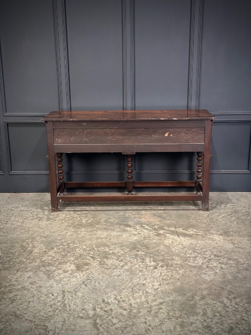 An antique oak dresser base featuring three drawers with geometric panel mouldings, turned front legs, and brass drop handles. View X